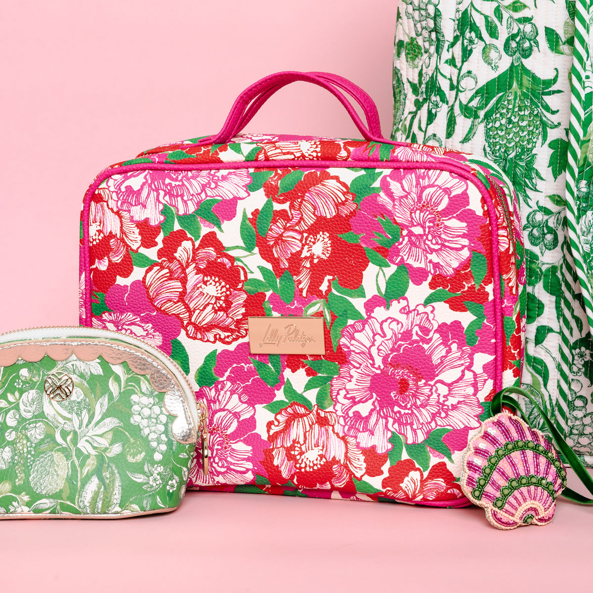up close of rectangular cosmetic bag with a vibrant pink, red, and green floral print on a cream background, featuring pink handles and a gold-tone brand plaque.