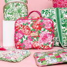 A rectangular cosmetic bag with a vibrant pink, red, and green floral print on a cream background, featuring pink handles and a gold-tone brand plaque. on a pink background surrounded by LP items