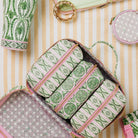 An open zippered cosmetic organizer bag filled with matching cylindrical pouches, shown in a styled flat-lay with other patterned accessories on a cream and tan striped surface.