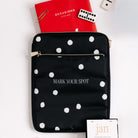 A black nylon tablet sleeve with white polka dots and the words 'MARK YOUR SPOT' printed in white, styled on a white background with a red notebook, paperclip, dice, and a hangtag.
