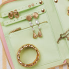 A mint green leather jewelry organizer pouch shown open, displaying gold jewelry including a twisted ring, shell-shaped drop earrings with pearl beads, and a zipper pocket.