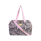A rectangular duffel bag with a black and white tropical leaf pattern, featuring light pink handles and a matching pink adjustable shoulder strap, with a small gold-tone metal plaque on the front.