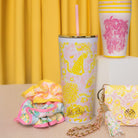 Colorful tumbler, keychain, and pouch with pink and yellow patterns on a yellow curtain background.