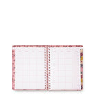 An open spiral-bound planner or agenda with pink floral-patterned covers and white interior pages featuring grid and lined sections, photographed on a plain white background.