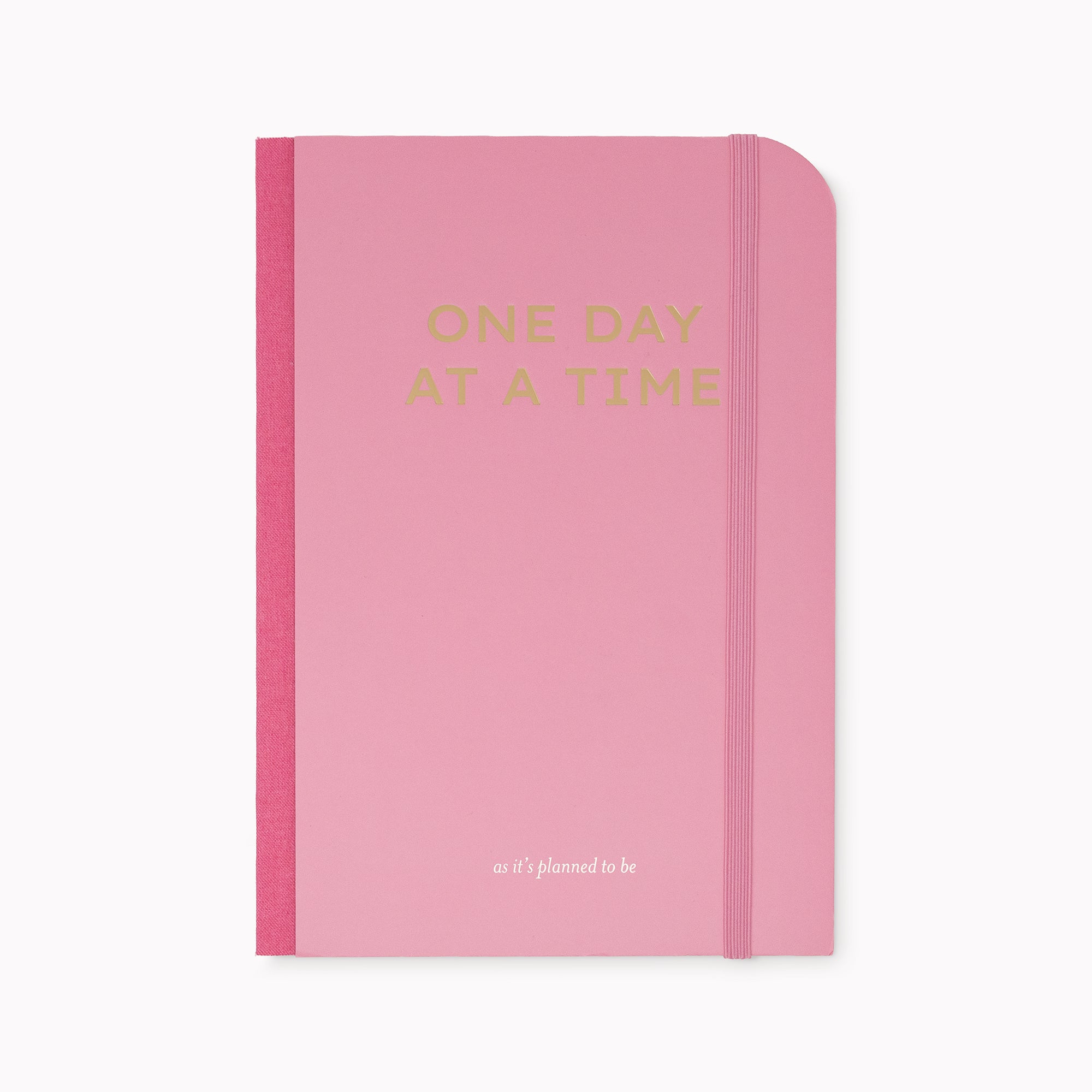 A pink hardcover planner with a matching pink elastic closure band. The front cover features the text 'ONE DAY AT A TIME' in a gold metallic font, with the brand name 'as it's planned to be' printed in small white script near the bottom.