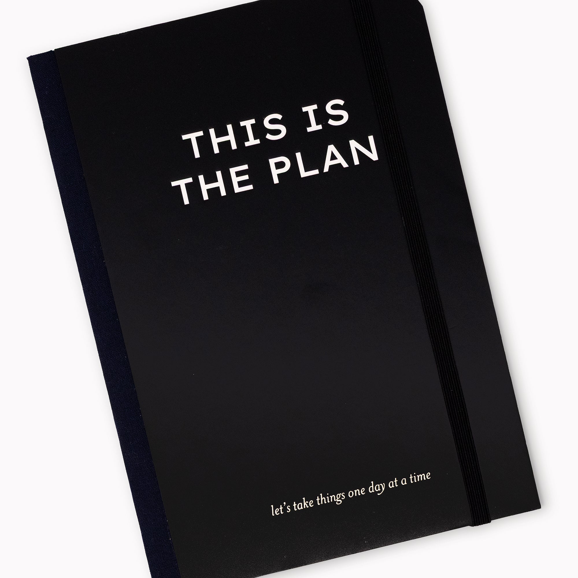 A black journal with white text reading 'THIS IS THE PLAN' and a smaller phrase near the bottom, shown on a clean white background.