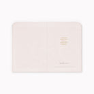 A black journal shown open flat against a white background, with small gold text on the right page and a faint brand mark near the bottom.