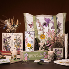 Collection of floral-themed products including tote bags, books, and candles on a dark surface.