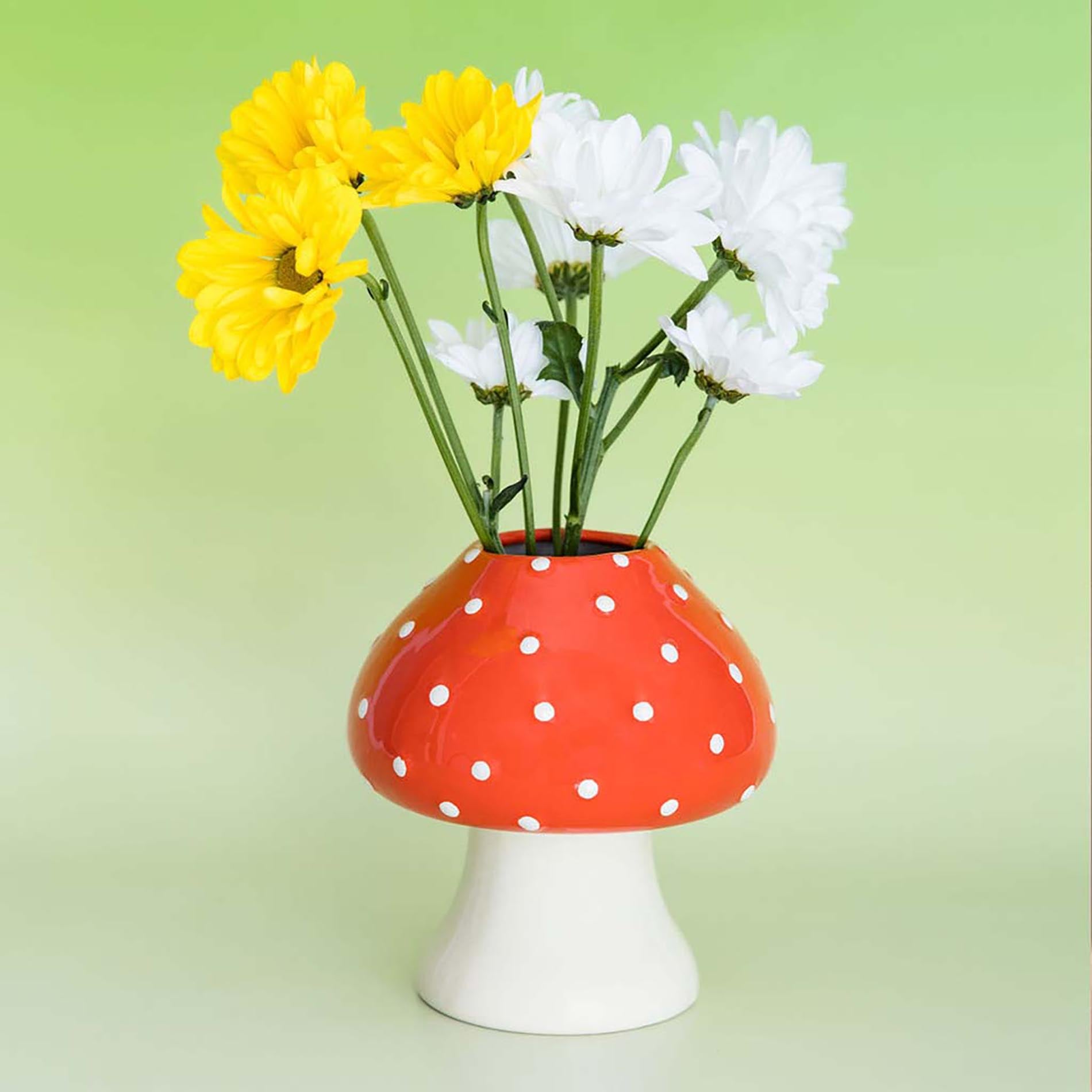 Red mushroom vase with yellow and white flowers on a green background