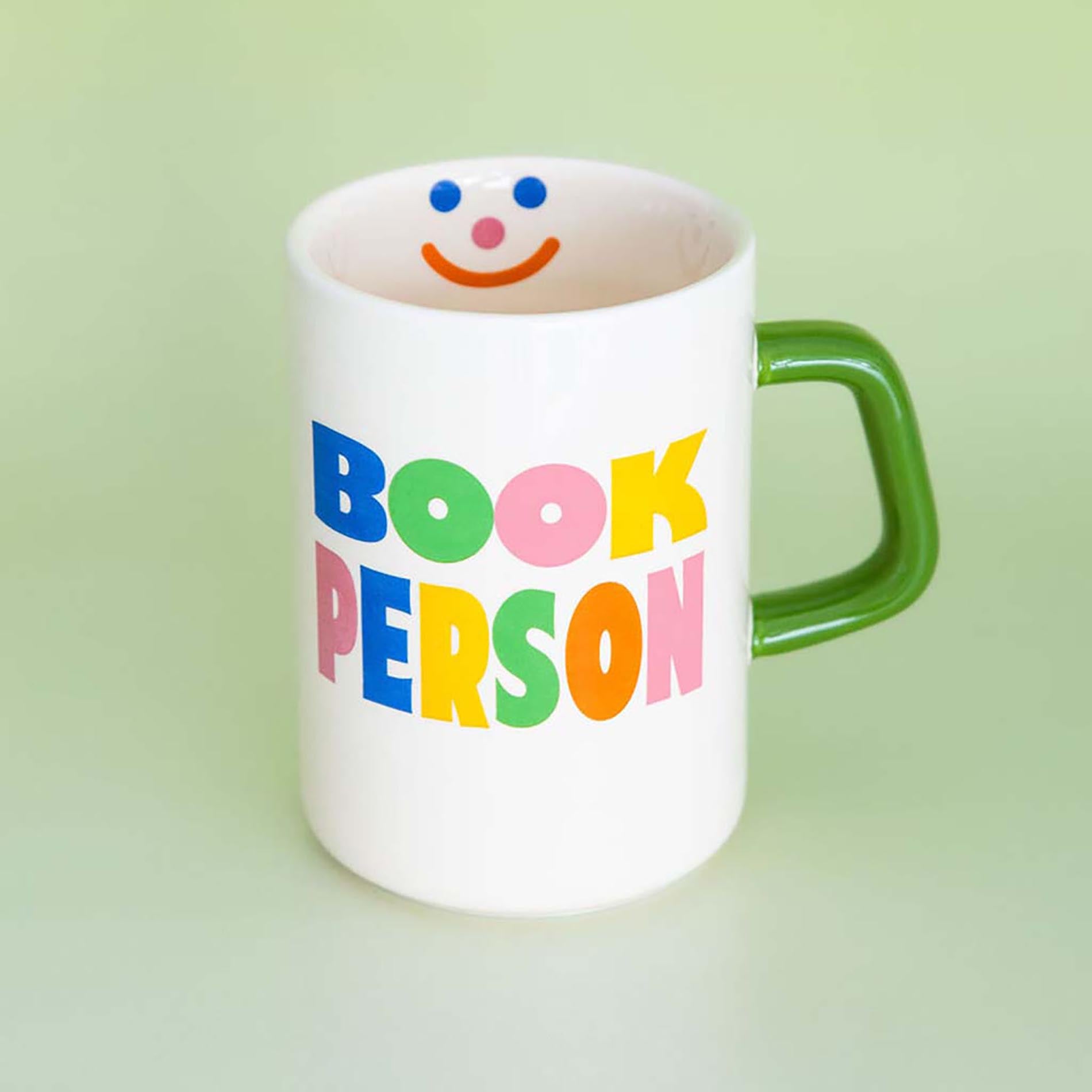 White mug with colorful 'BOOK PERSON' text and a green handle on a light green background