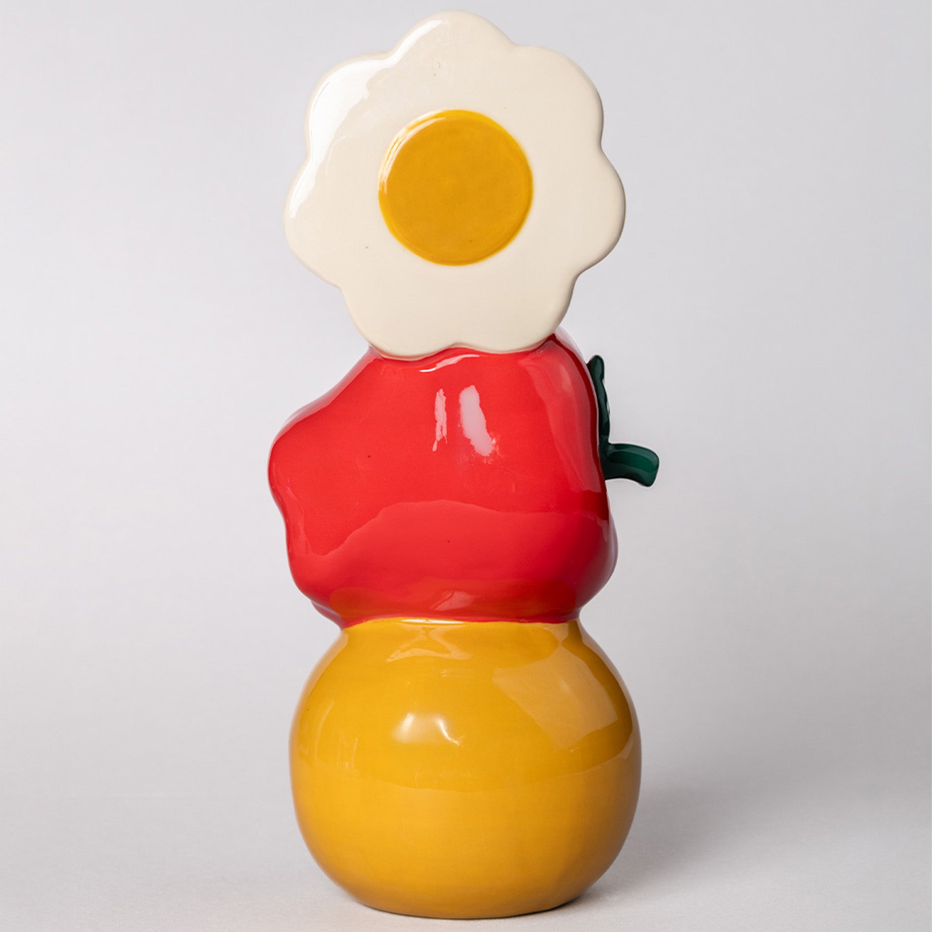 Colorful ceramic vase with a red apple, yellow smiley, and daisy on top against a light gray background