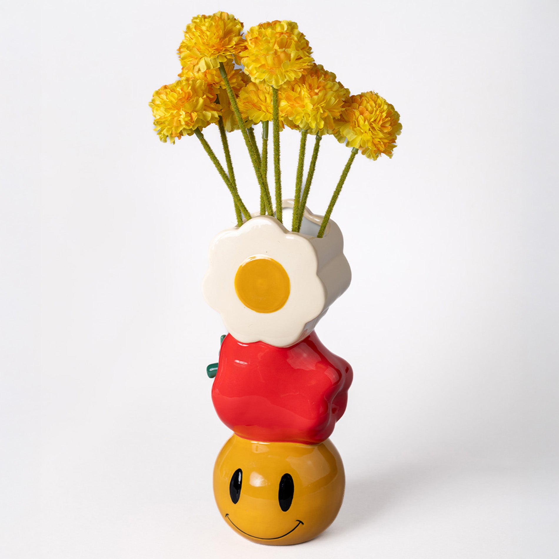 Colorful vase shaped like a smiley face with yellow flowers on a white background