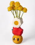 Colorful vase shaped like a smiley face with yellow flowers on a white background