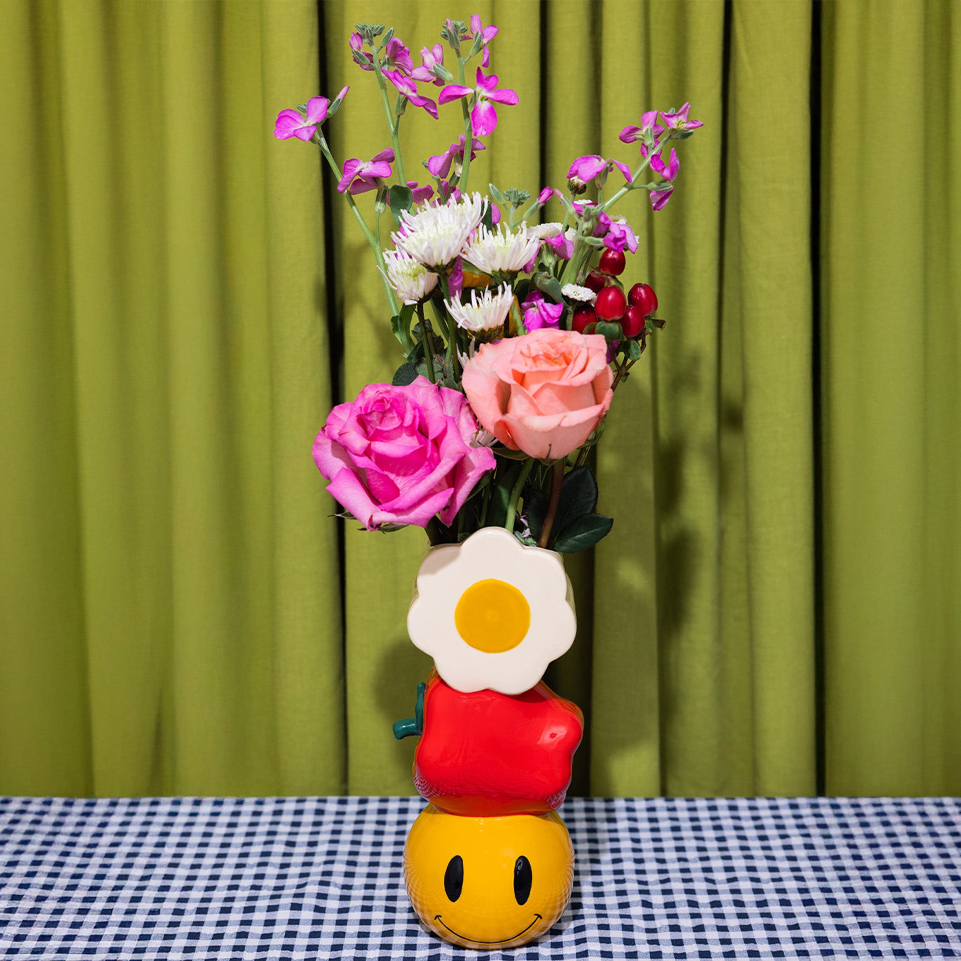 Colorful flower arrangement in a unique vase with a checkered tablecloth and green curtain background
