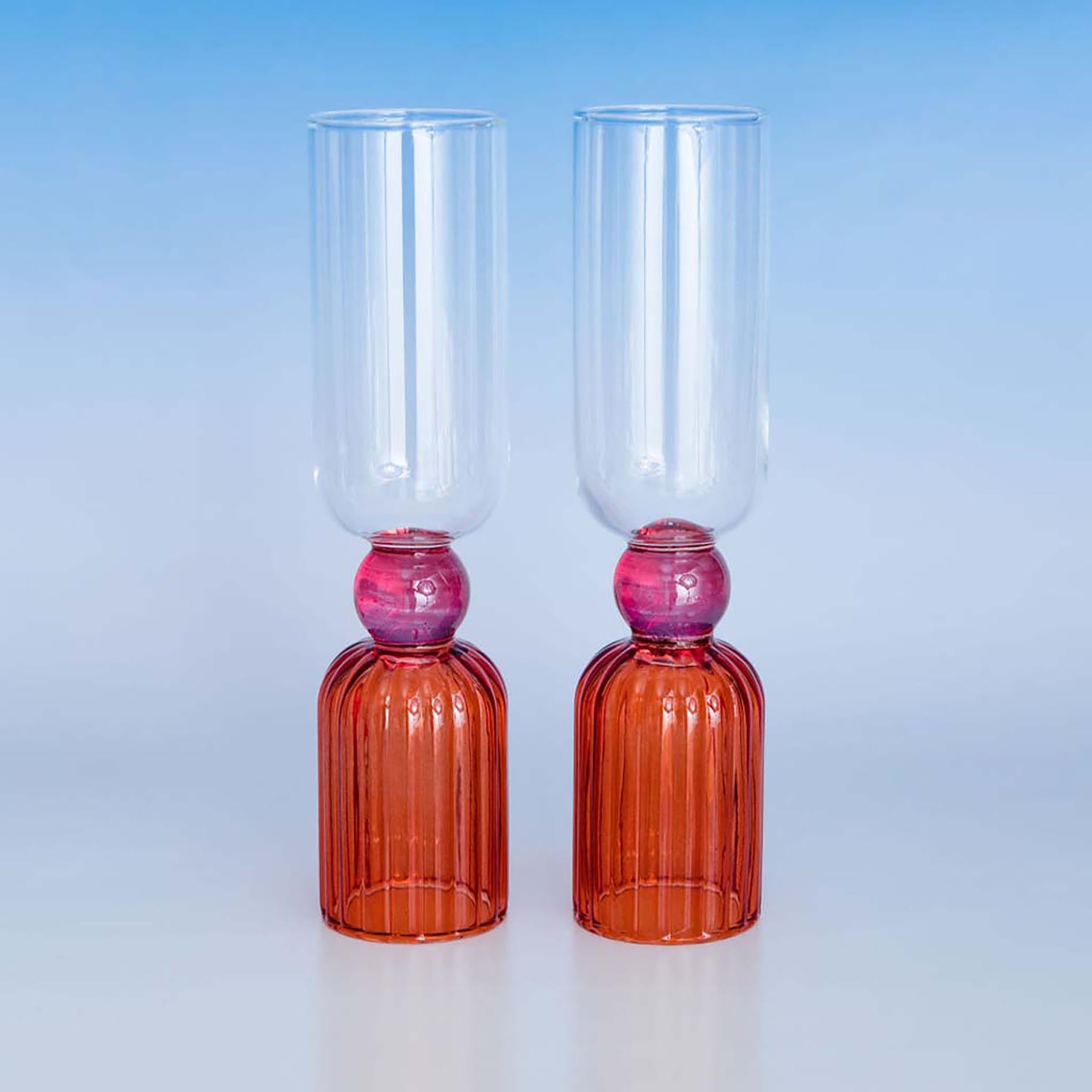 Two glass goblets with red bases and pink beads on a light blue background
