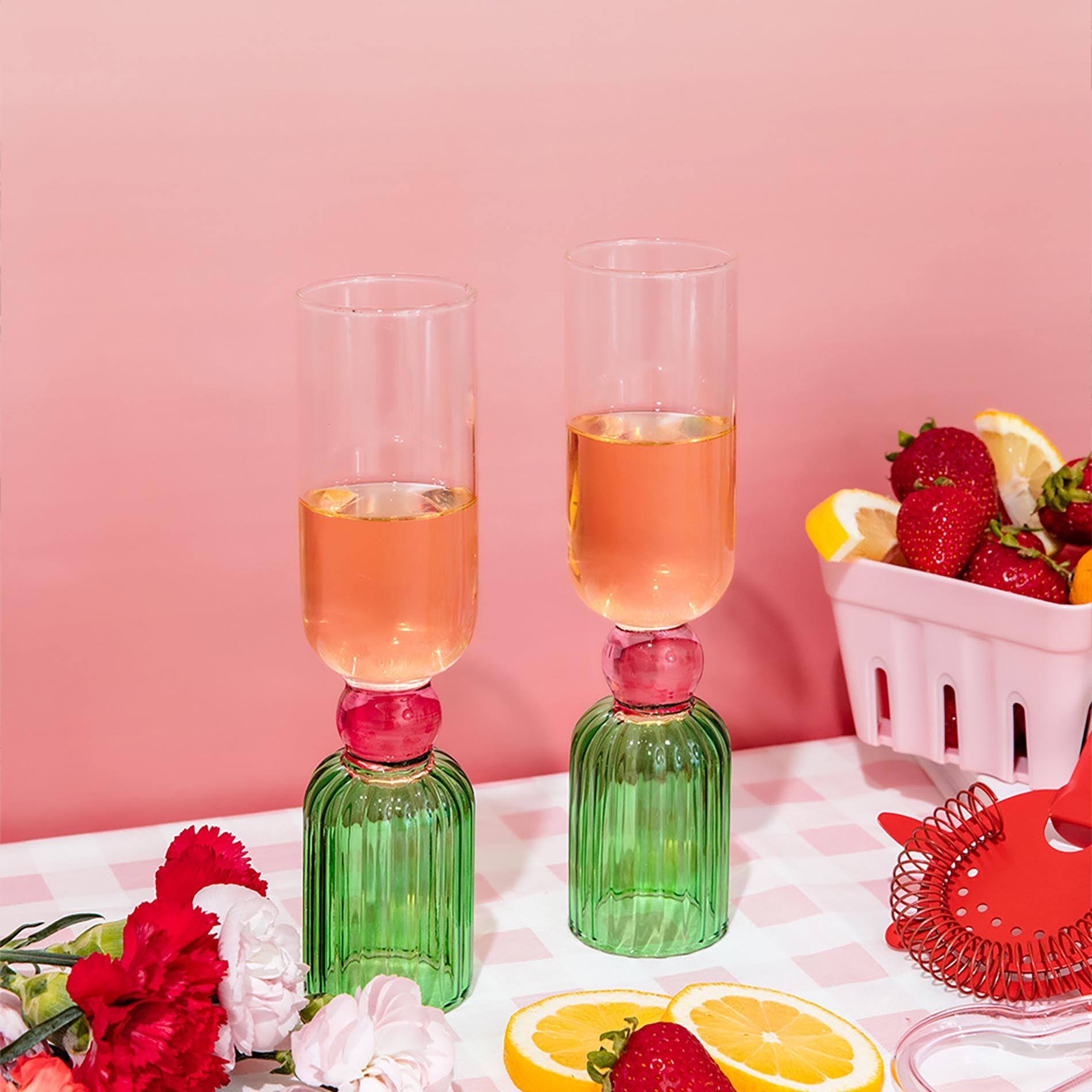 Two green glasses with pink liquid on a checkered tablecloth with strawberries and lemons.
