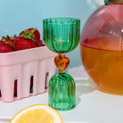 Green glass shot glass with yellow heart center on a white surface.