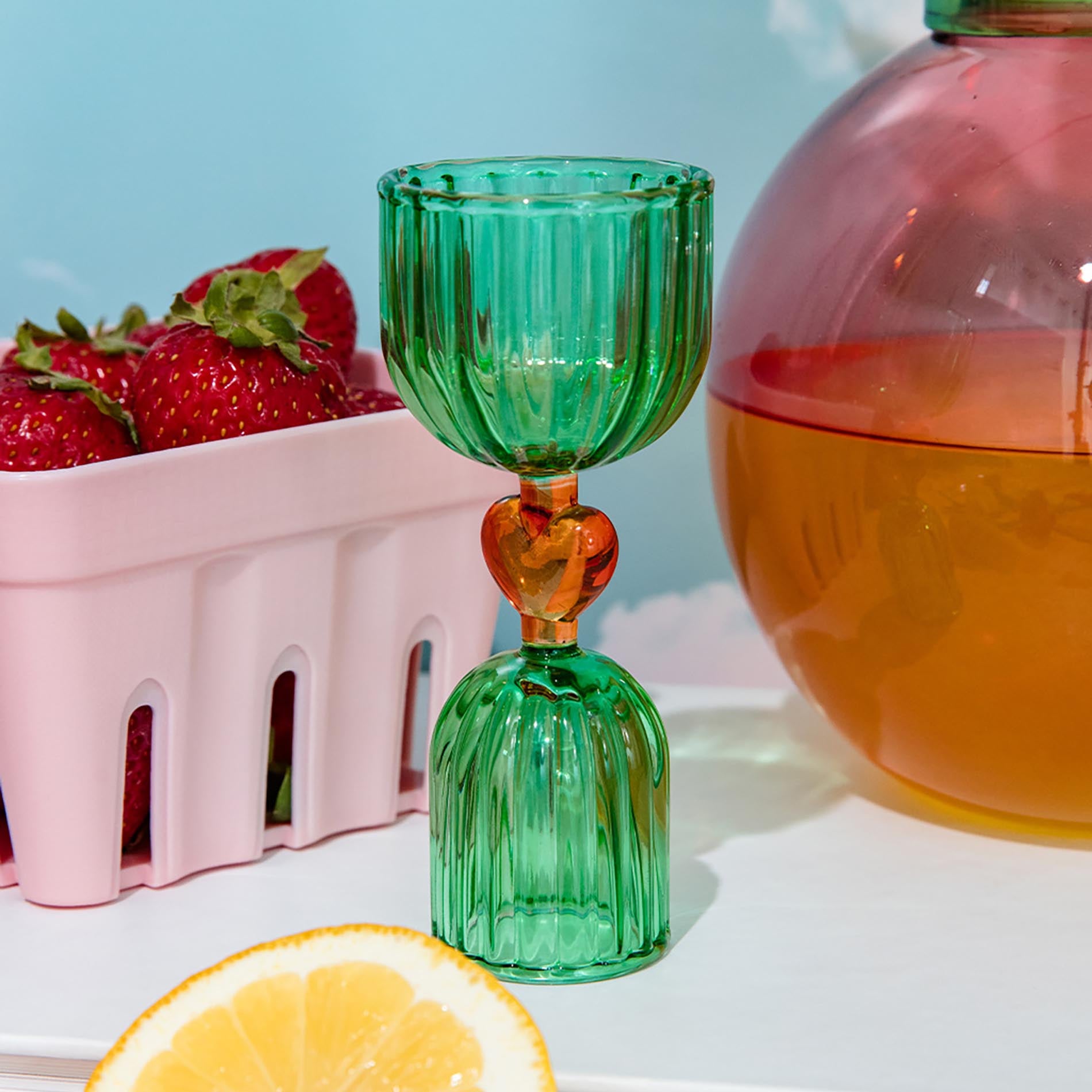 Green glass shot glass with yellow heart center on a white surface.