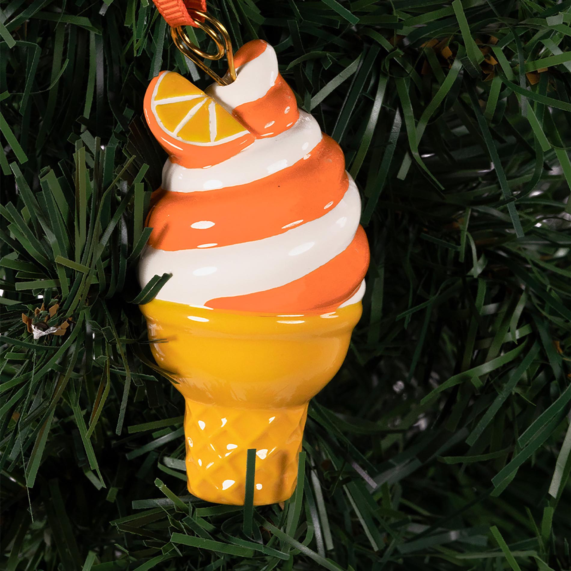 Ice cream cone ornament with orange and white swirls hanging on a Christmas tree.