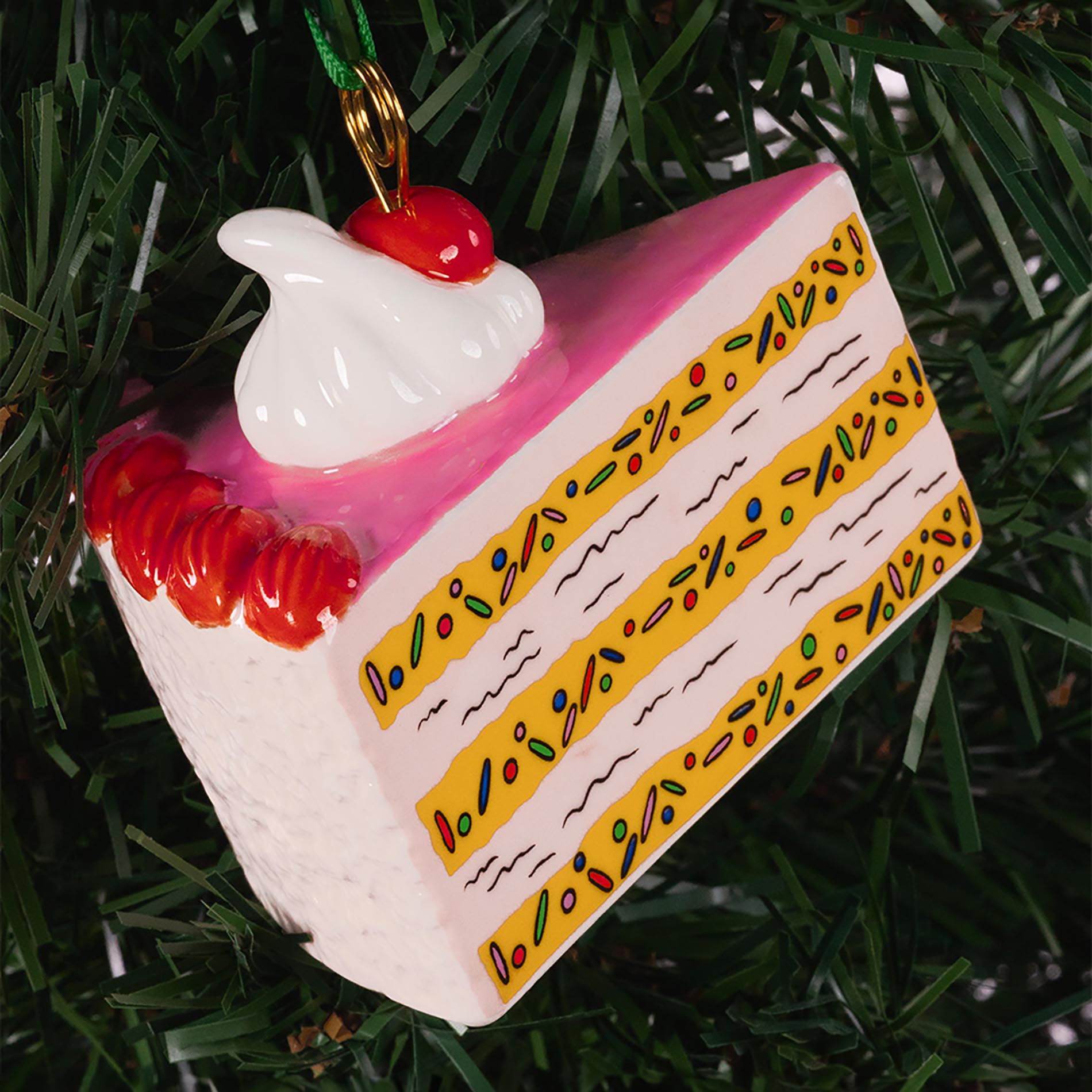 Decorative cake slice ornament with cherry on top hanging on a Christmas tree.