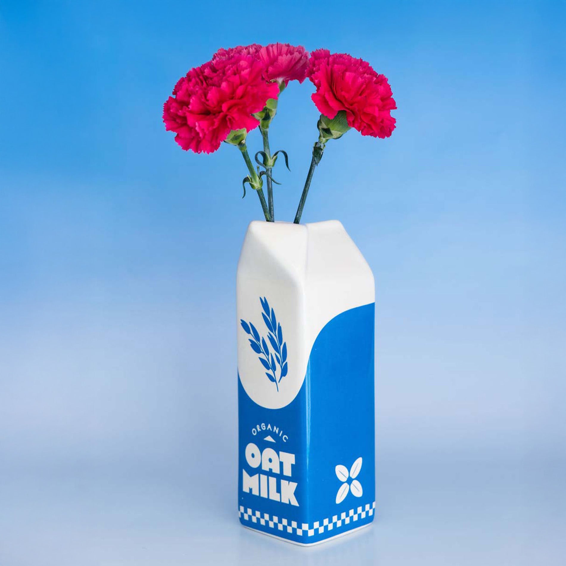 Oat milk carton vase with pink flowers against a blue gradient background