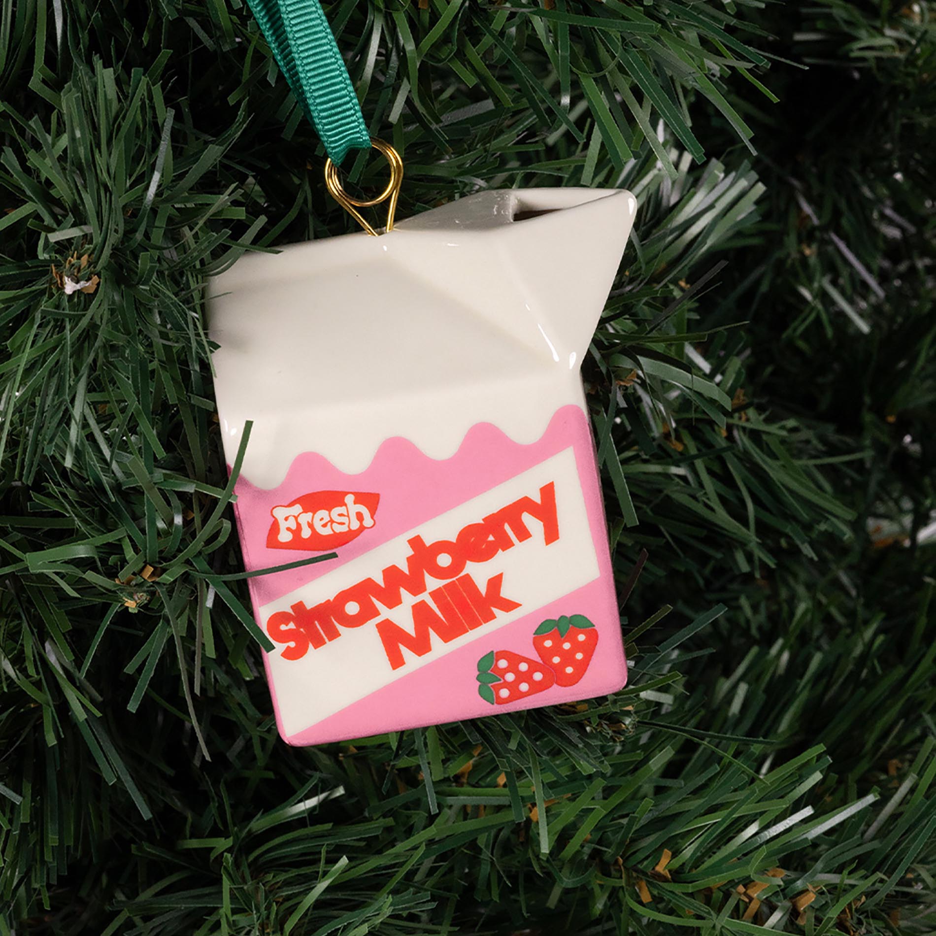 Decorative ornament shaped like a strawberry milk carton hanging on a Christmas tree.