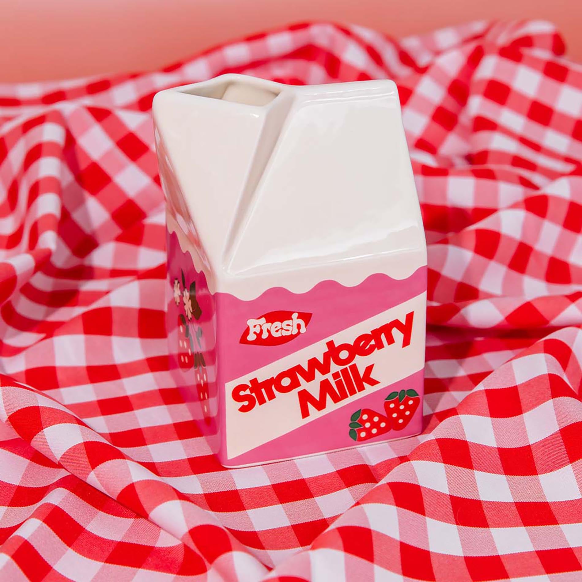 Carton of strawberry milk vase on a red and white checkered tablecloth