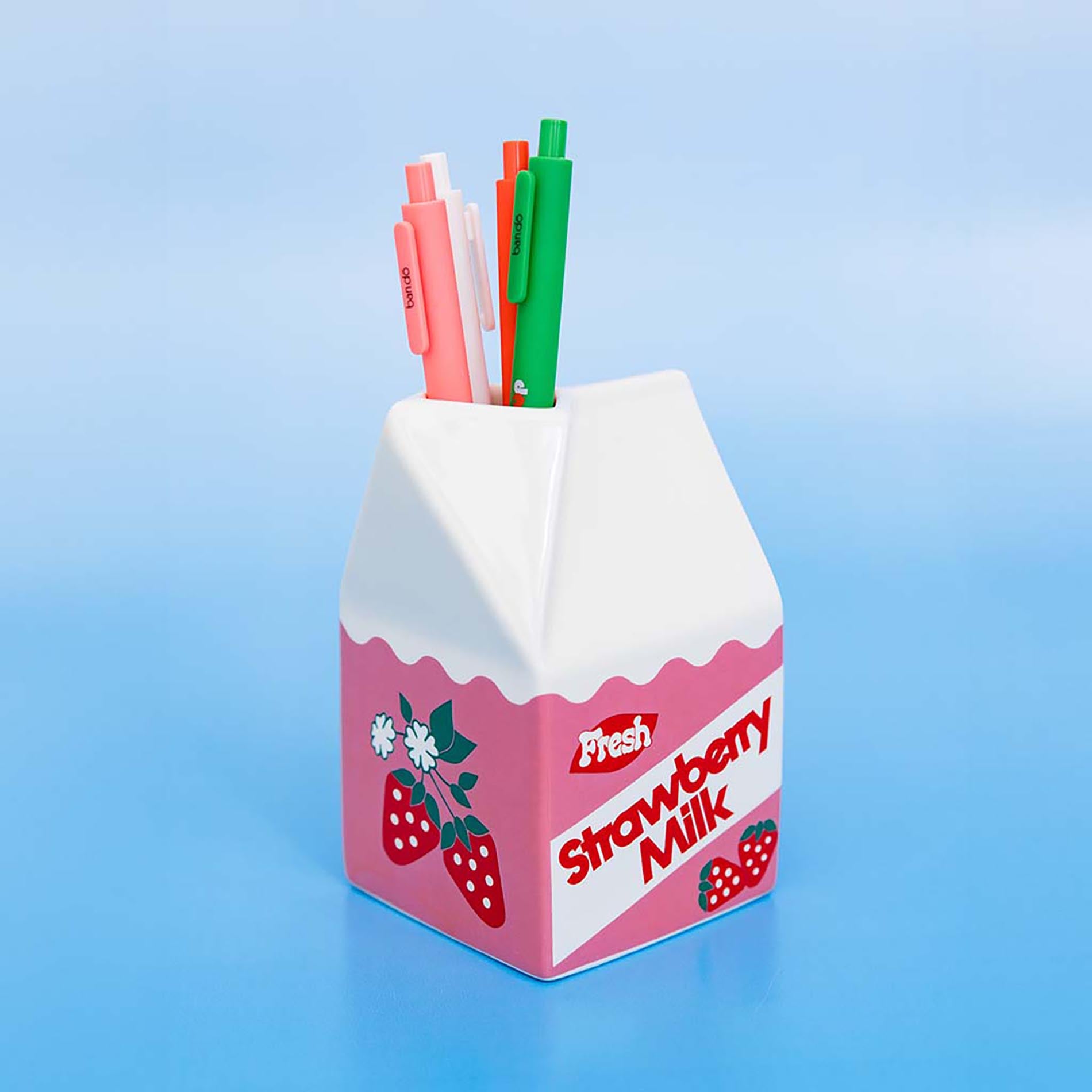 Strawberry milk carton-shaped pen holder with pens on a blue background