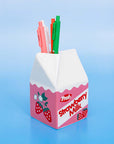 Strawberry milk carton-shaped pen holder with pens on a blue background