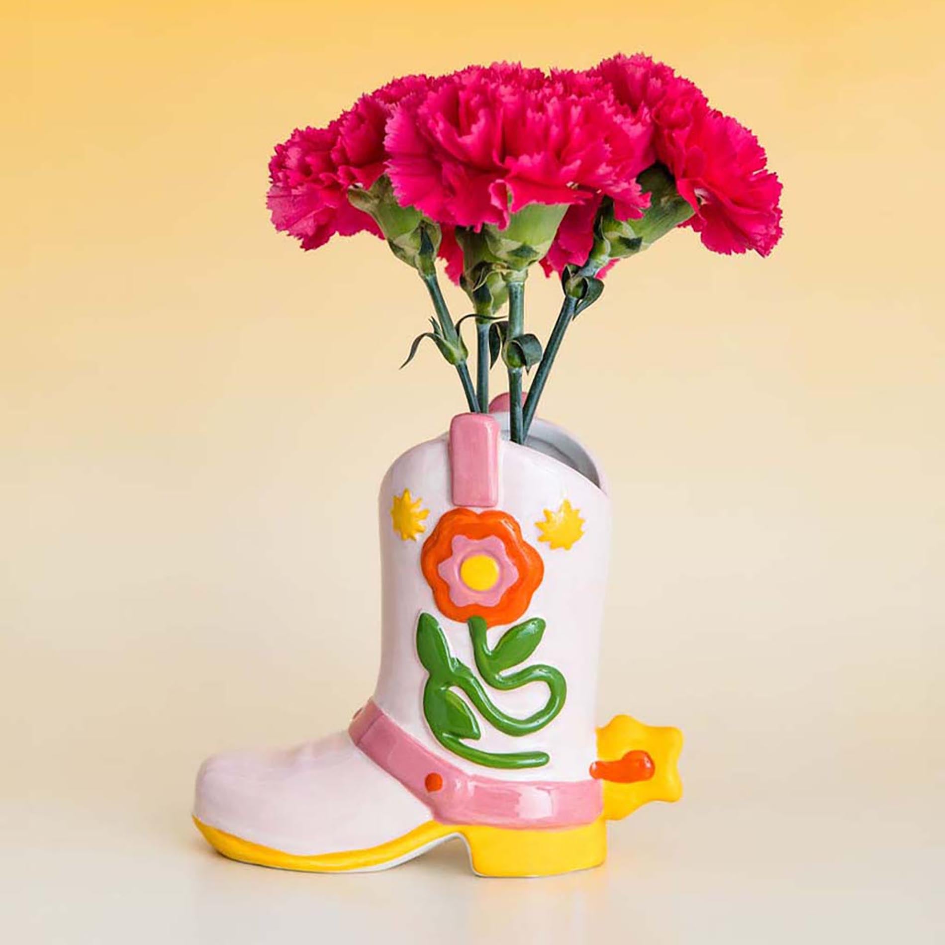 Decorative boot-shaped vase with pink flowers on a yellow background