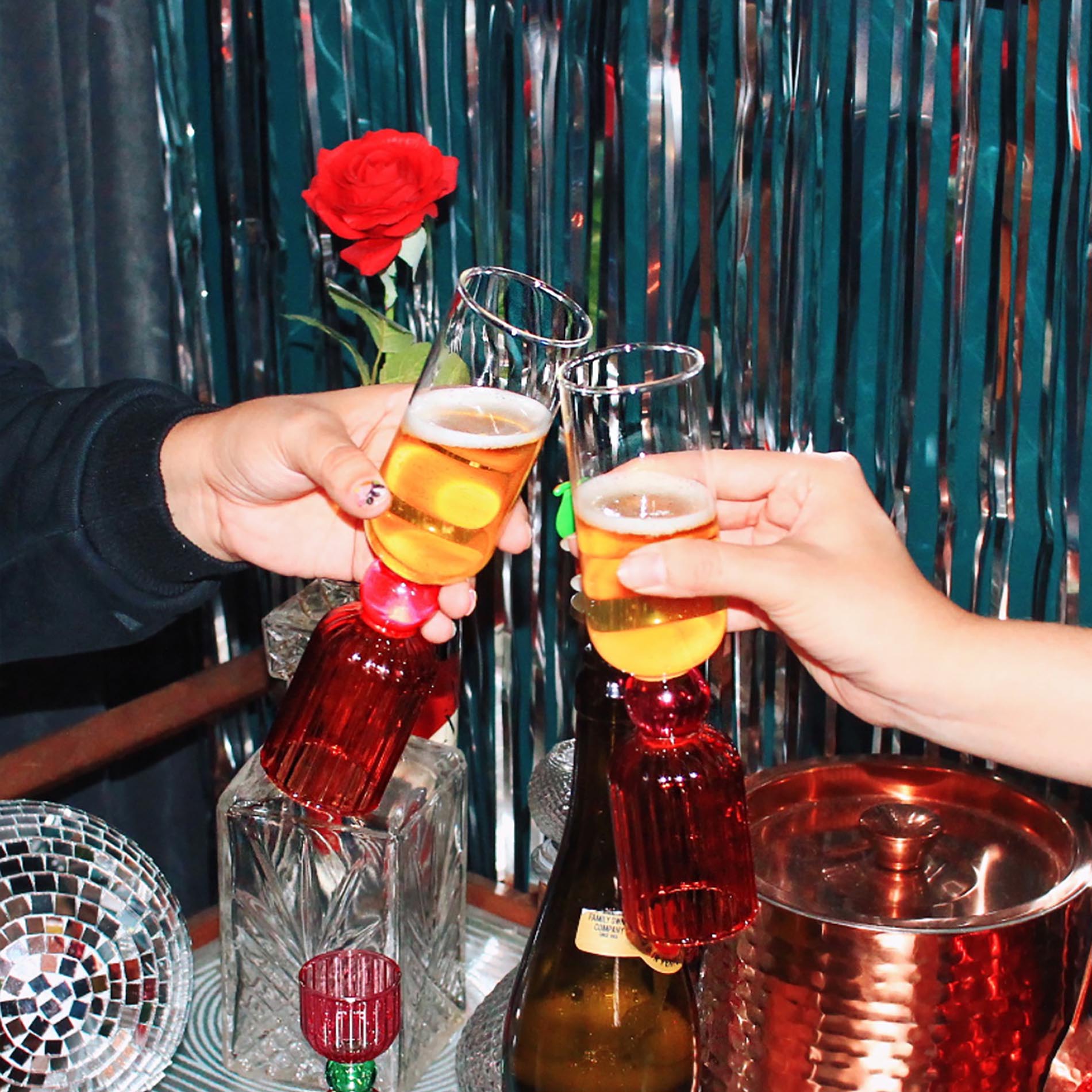 Two people clinking glasses with a decorative red rose in the background.