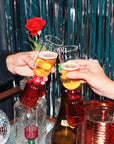 Two people clinking glasses with a decorative red rose in the background.
