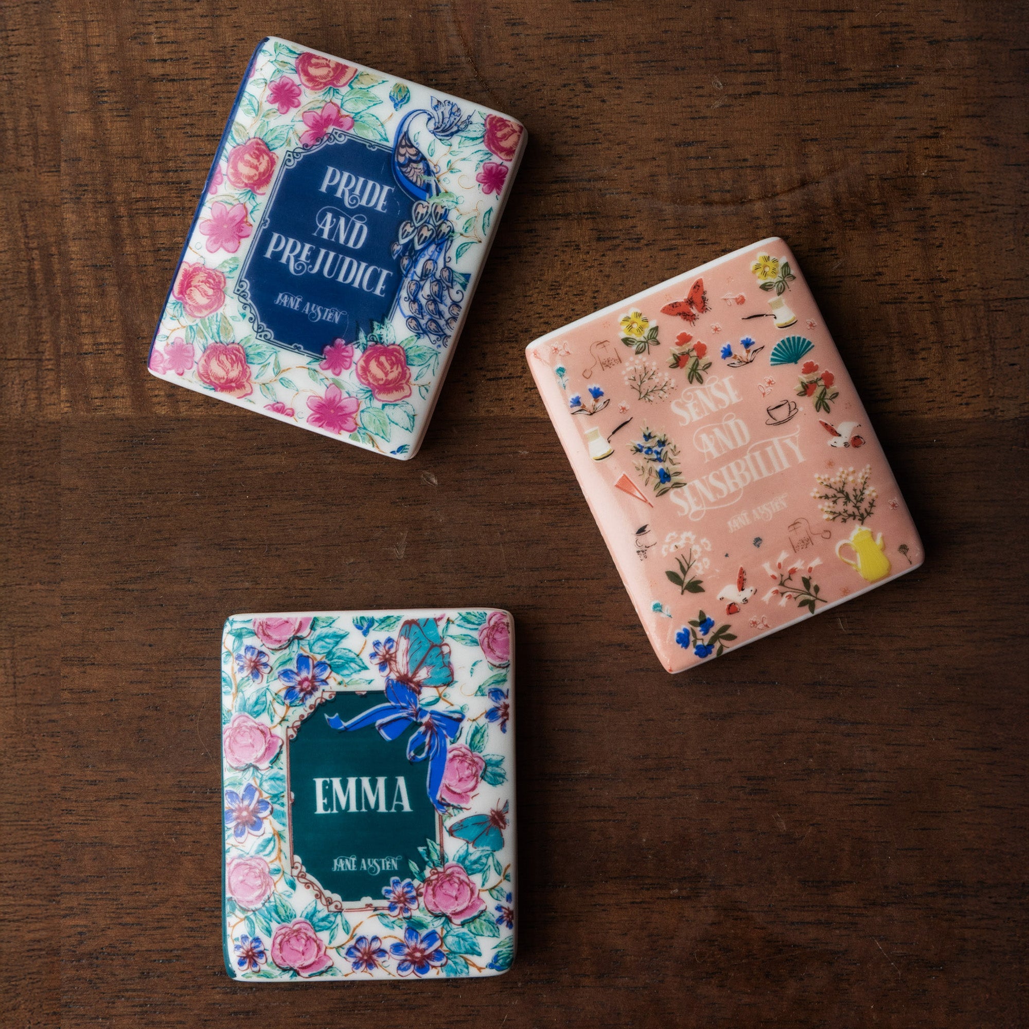 Three book-themed magnets with floral designs and book titles on a white background