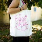 model carrying white tote with pink strap and lettering that says 'I love you...thorns and all' with a sketched floral print