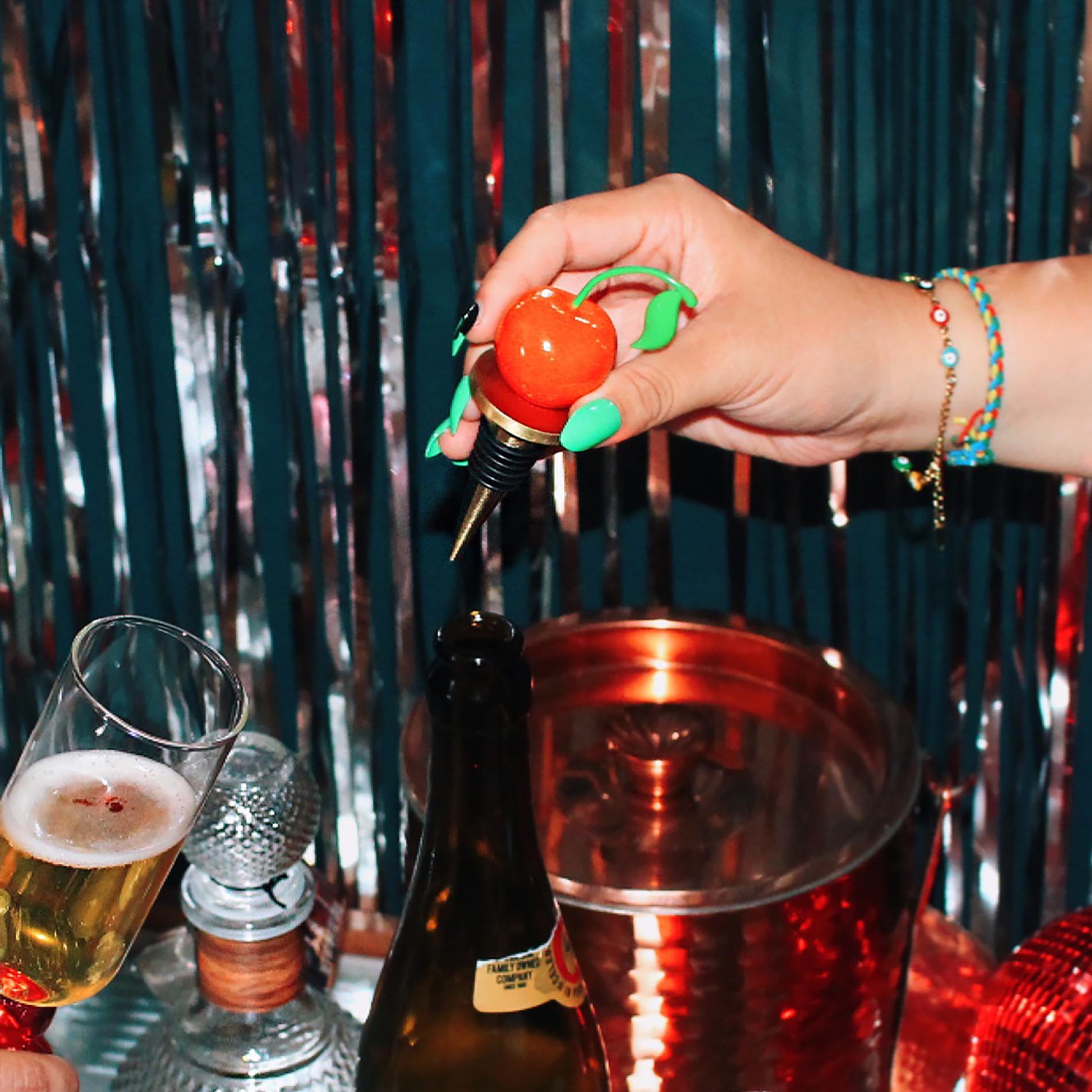 Hand using a cherry-themed bottle opener on a bottle with a festive background