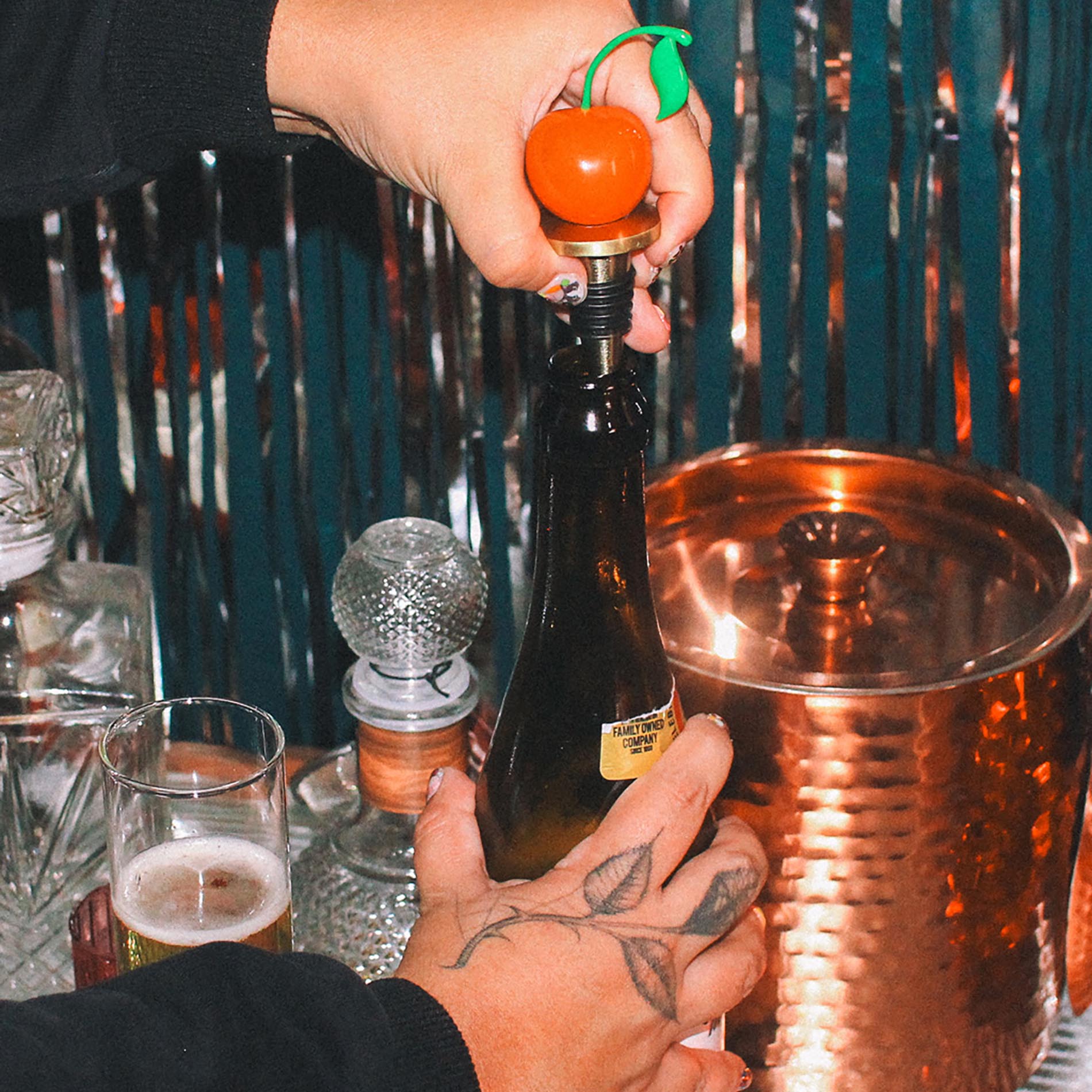 Person opening a bottle with a decorative bottle opener at a bar.
