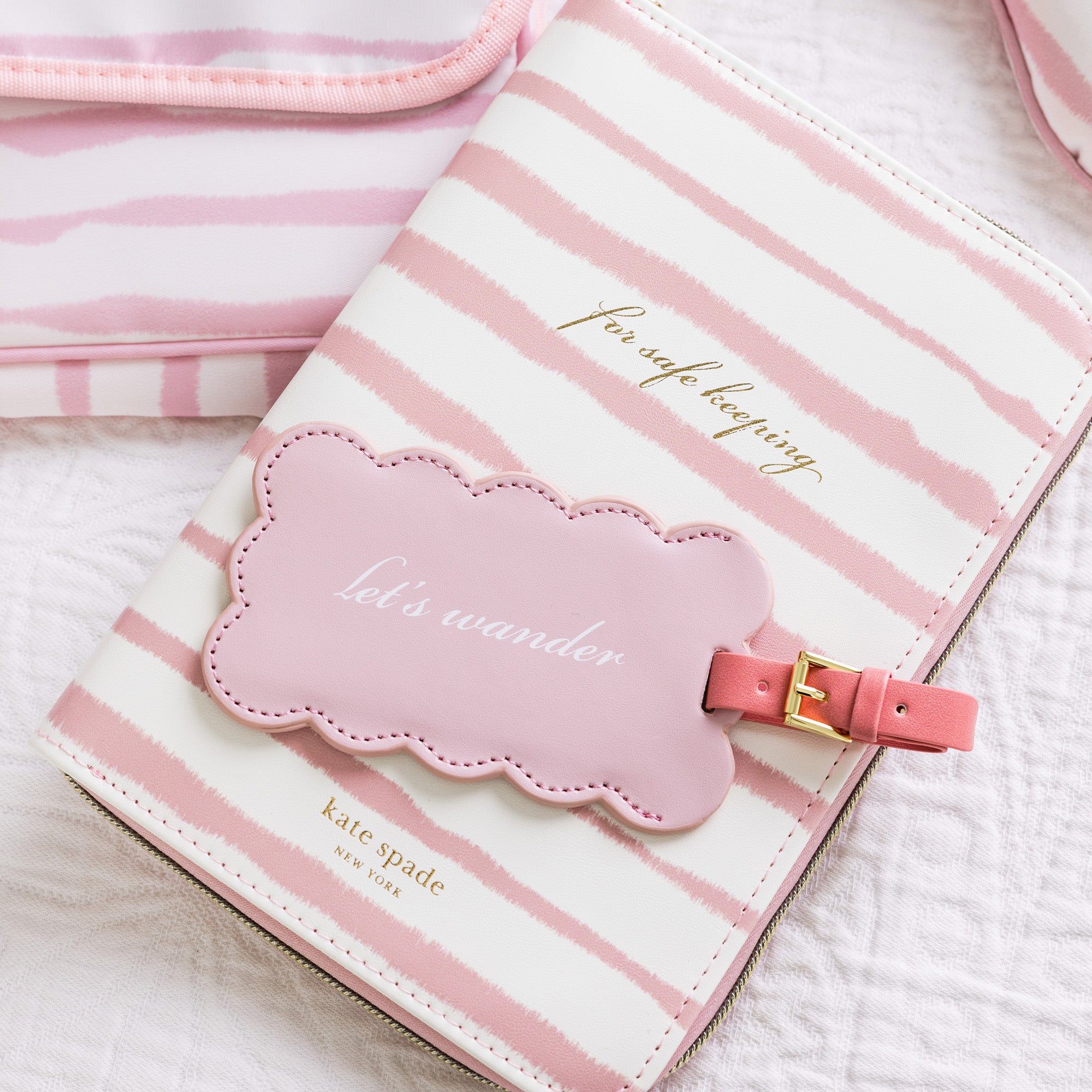Pink and white striped travel pouch with a cloud-shaped tag on a light background