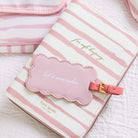 Pink and white striped travel pouch with a cloud-shaped tag on a light background