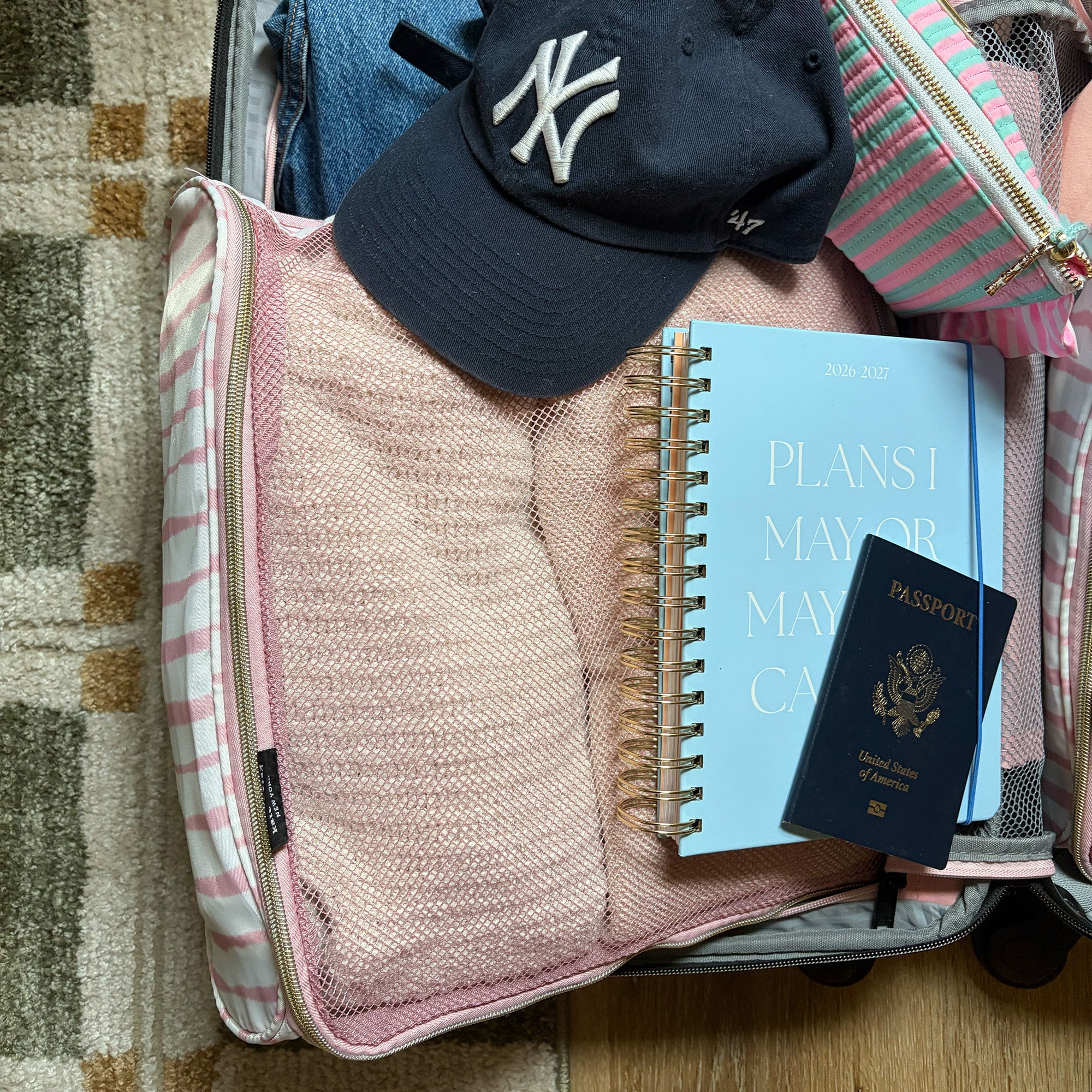 pink and white striped packing cube set with a hat, book, planner, passport and clothes inside