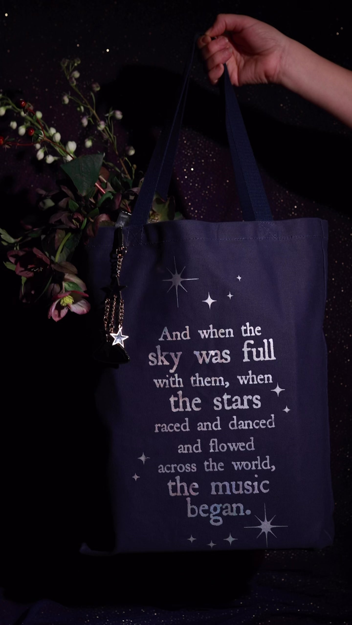 model showcasing model showcasing navy tote that says 'AND WHEN THE SKY WAS FULL WITH THEM, WHEN THE STARS RACES AND DANCED AND FLOWERS ACROSS THE WORLD, THE MUSIC BEGAN'