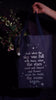 model showcasing model showcasing navy tote that says 'AND WHEN THE SKY WAS FULL WITH THEM, WHEN THE STARS RACES AND DANCED AND FLOWERS ACROSS THE WORLD, THE MUSIC BEGAN'