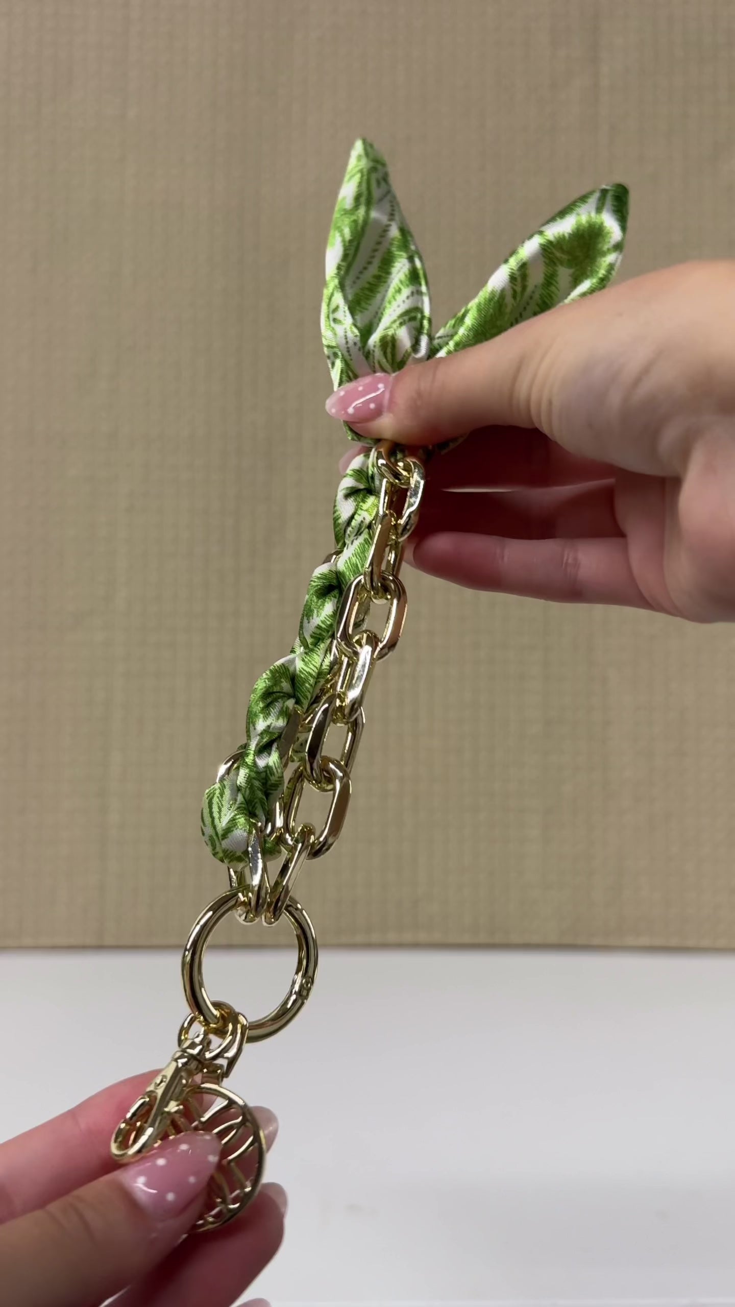 model showcasing A gold chain bracelet with a green and white patterned silk scarf tied in a knot, featuring a circular geometric charm and lobster clasp, shown on a plain white background.