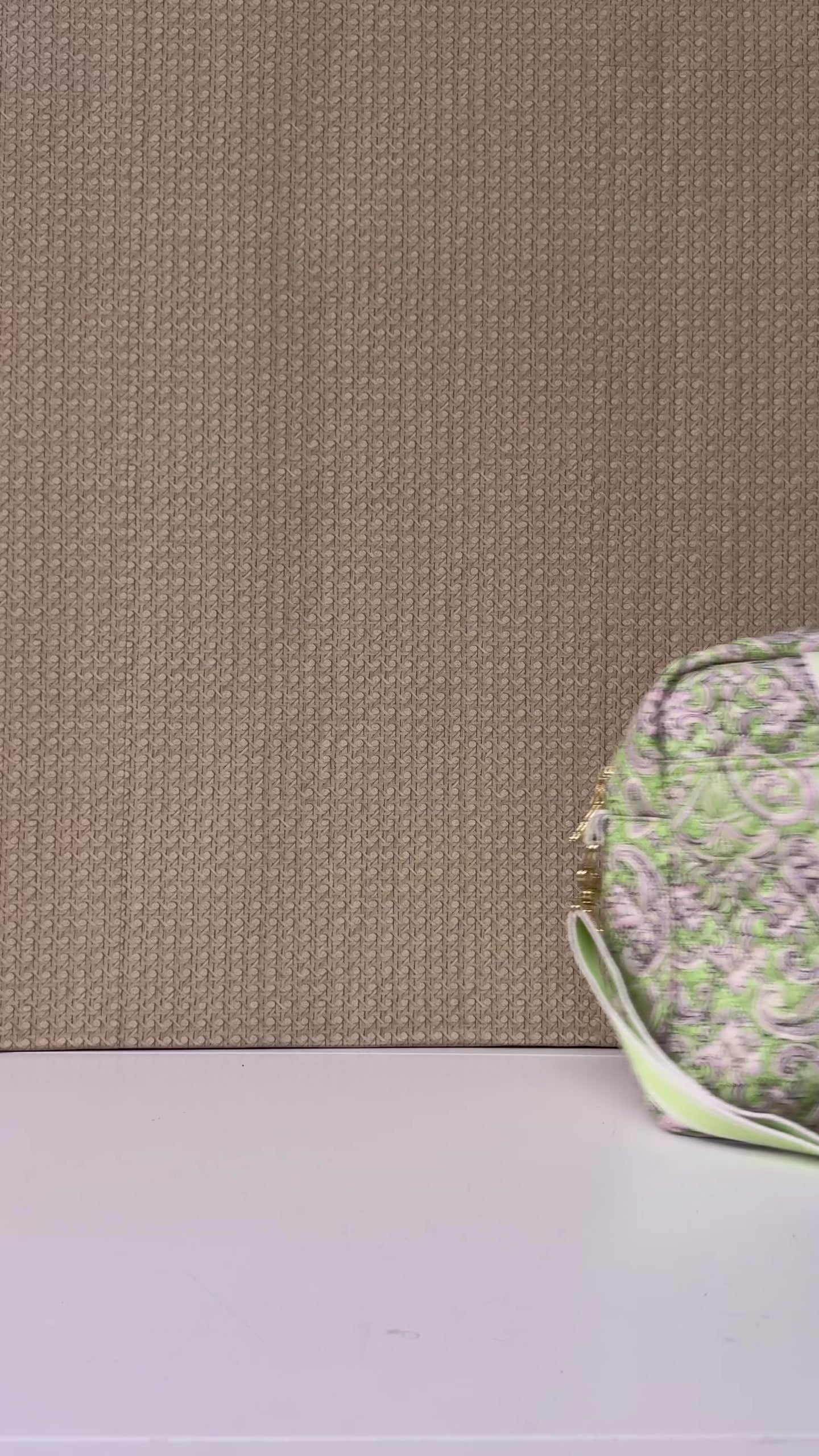 model showcasing quilted travel bag featuring a light green and pink paisley pattern, with matching green and white striped handles and a green adjustable shoulder strap, shown on a plain white background.