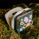 side view of small kiss-lock coin purse with a cream-colored frame and zipper, featuring a dark green front panel decorated with a colorful floral print of pink, orange, yellow, and white flowers.