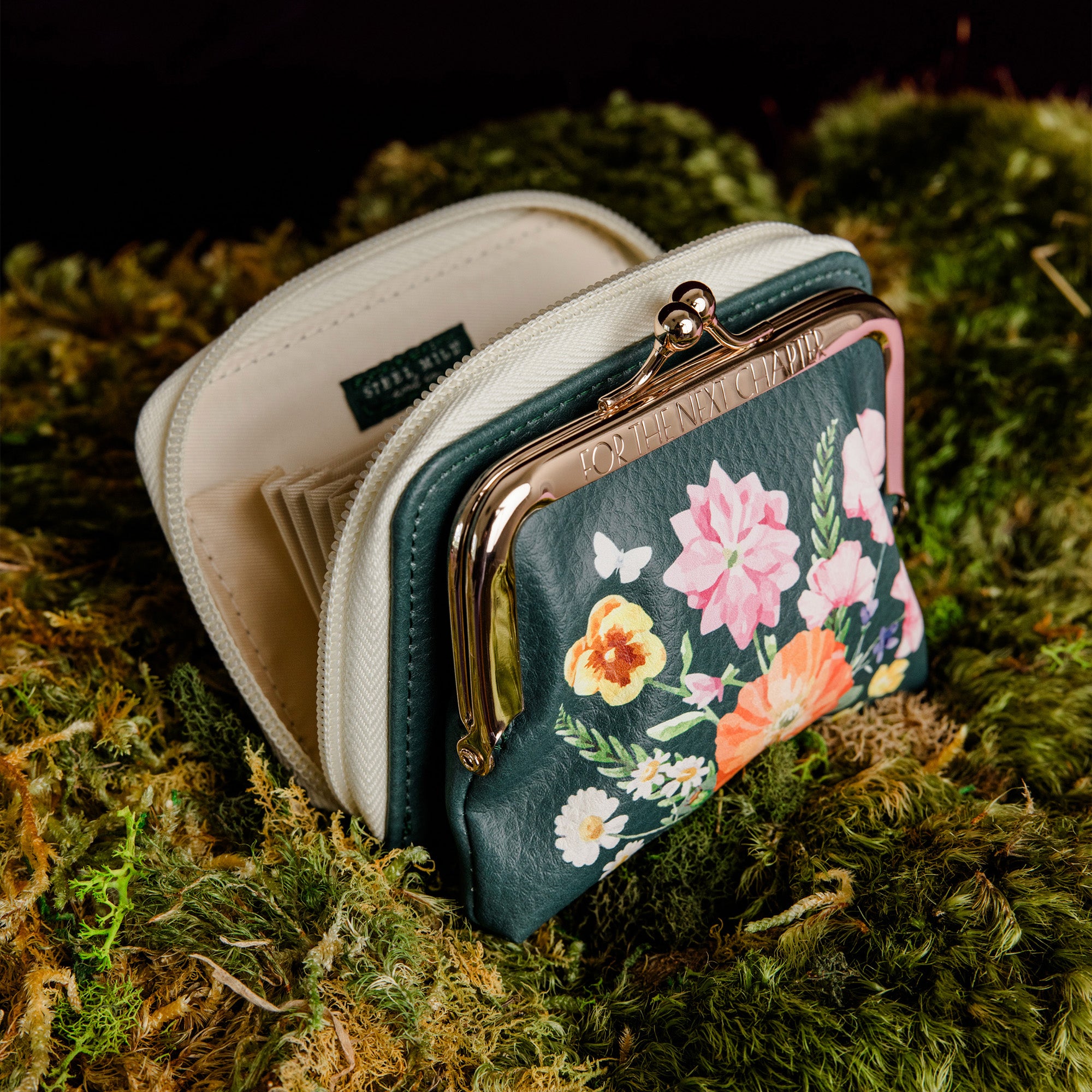 side view of small kiss-lock coin purse with a cream-colored frame and zipper, featuring a dark green front panel decorated with a colorful floral print of pink, orange, yellow, and white flowers.