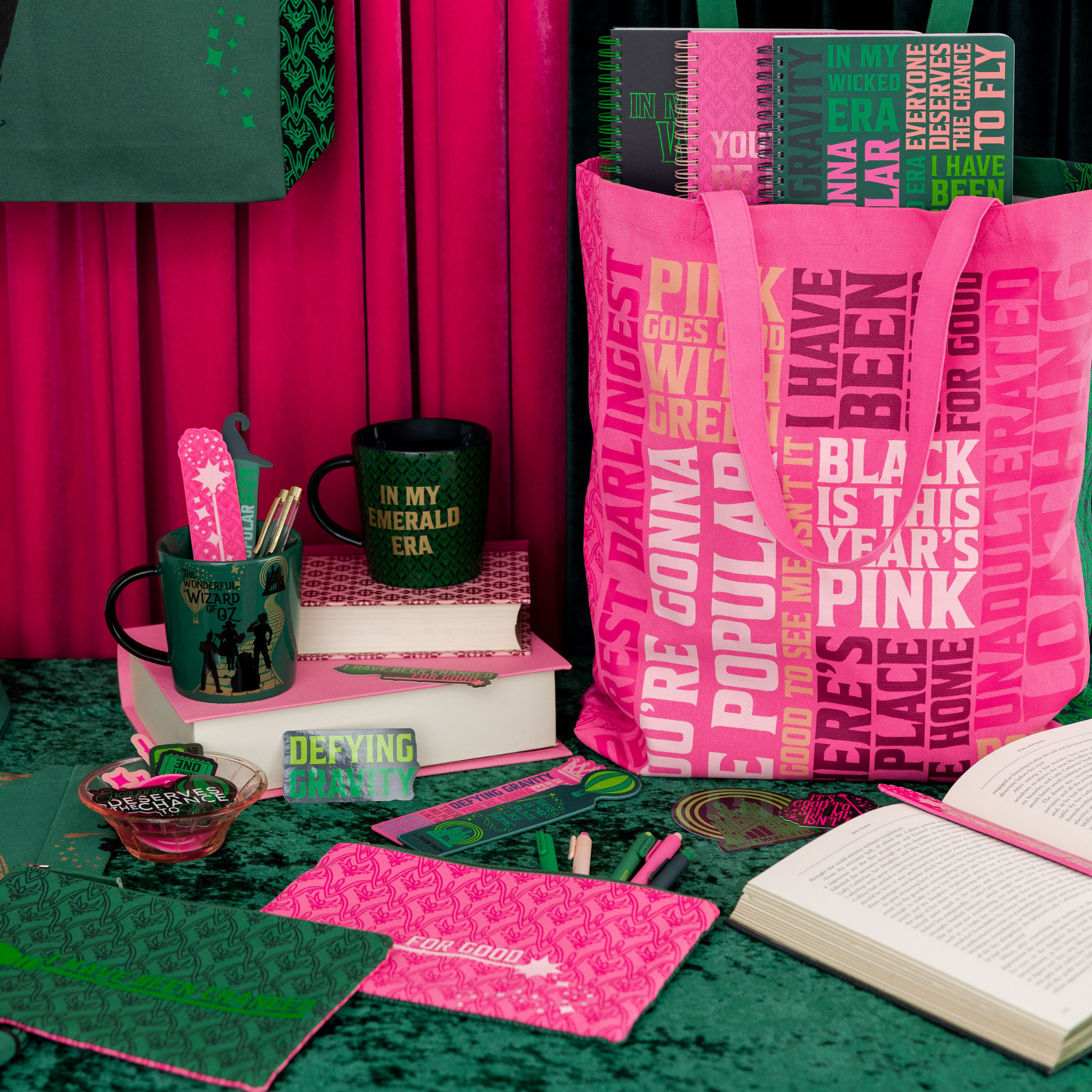 Pink and green stationery items including notebooks, a bag, and books on a green surface with pink background.