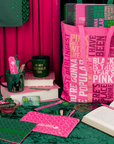Pink and green stationery items including notebooks, a bag, and books on a green surface with pink background.
