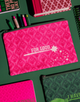 Pink pouch with 'FOR GOOD' text on a green background with stationery items.