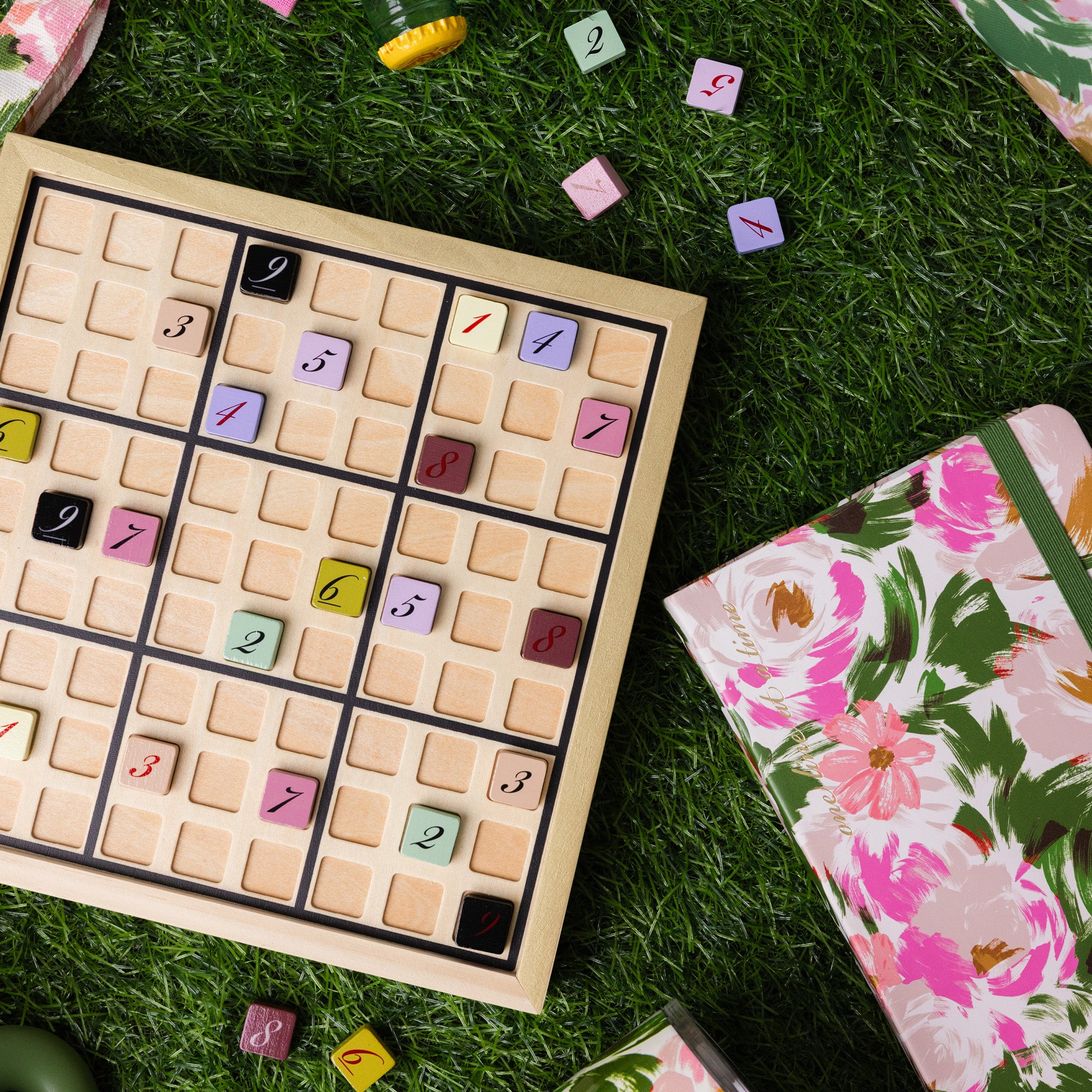 Sudoku board with colored numbers on grass, next to a floral notebook