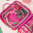 A twisted fabric headband featuring a vibrant pink floral print with green leaves, decorated with gold-tone beads and dark red jewel embellishments in a travel case
